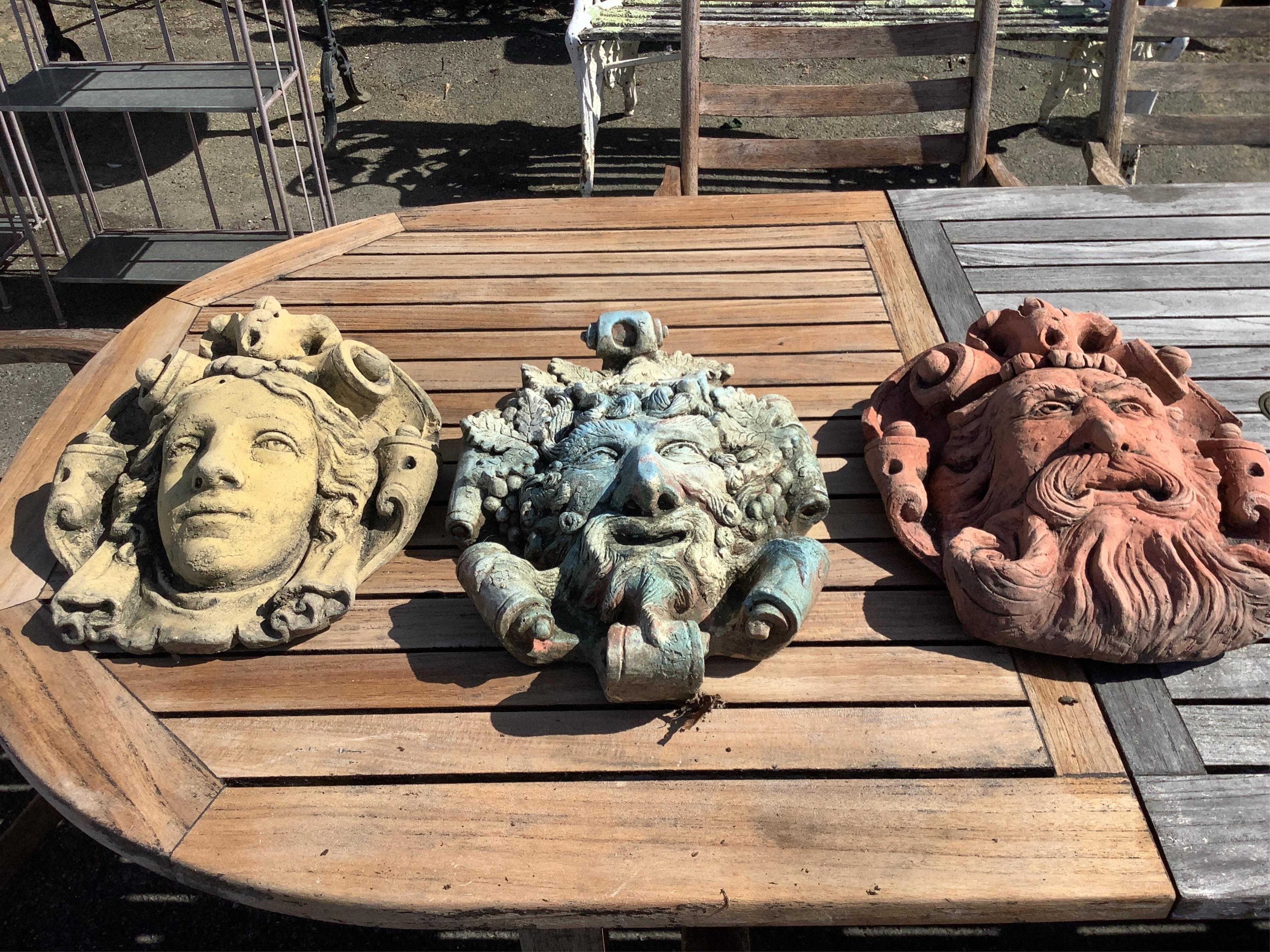Three cast stone and terracotta garden wall mask appliqués, largest height 42cm